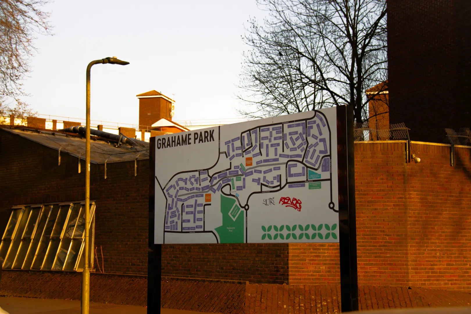 Map sign for Grahame Park against a brick building, surrounded by bare trees.