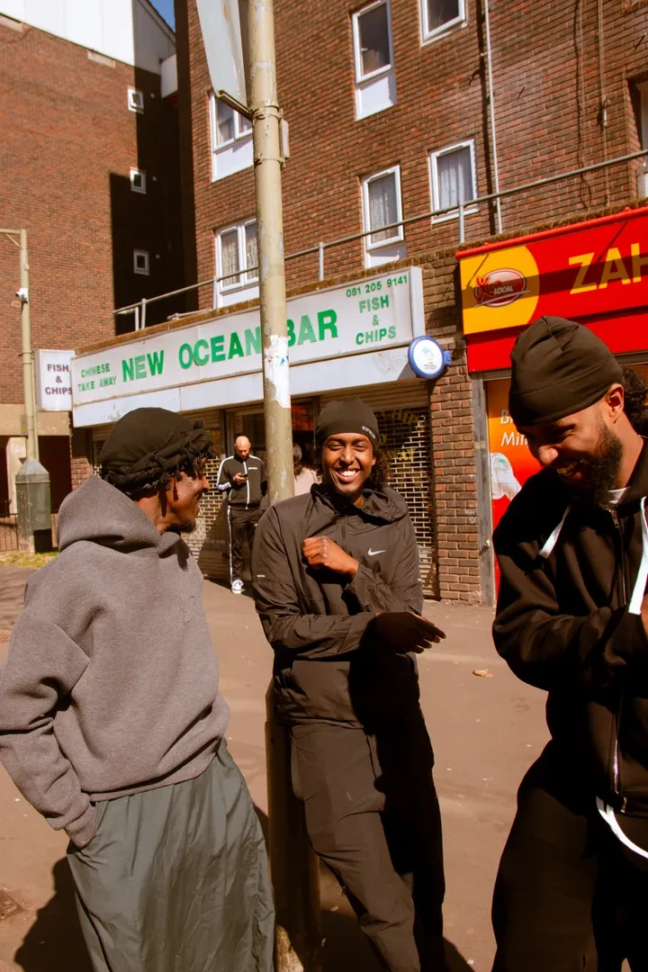 A small group of three young people are sharing a laugh in an urban environment with a take-away in the background.